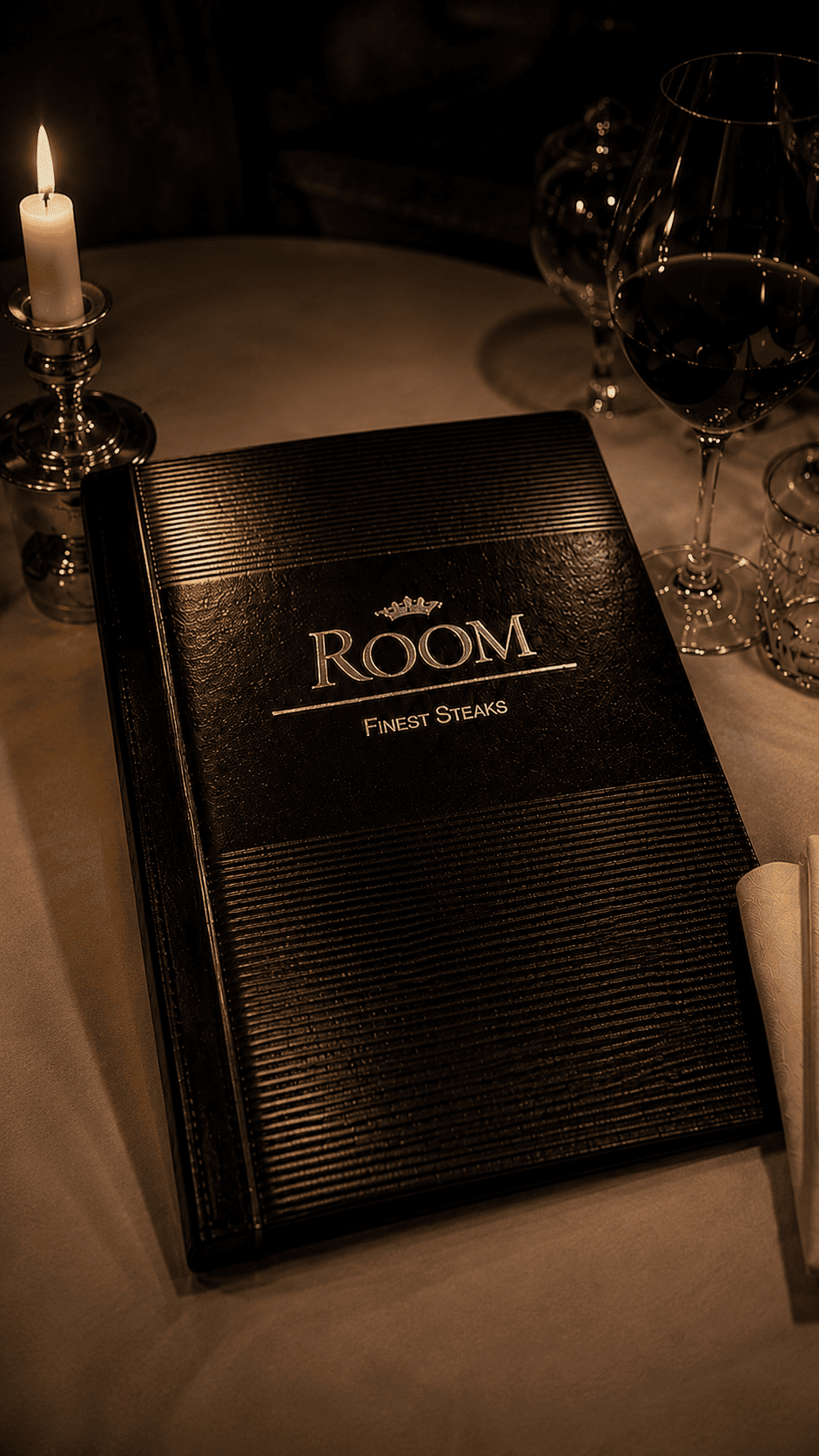 Das schwarze Menübuch von Restaurant ROOM auf weißer Tischwäsche, daneben Kerze und Rotwein